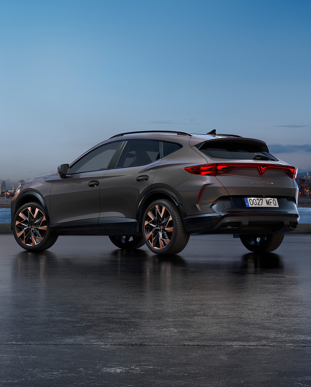 A new CUPRA Formentor 2024 graphene grey CUV parked on a waterfront promenade during twilight. The background features a cityscape with skyscrapers and palm trees illuminated by the fading light of the day.