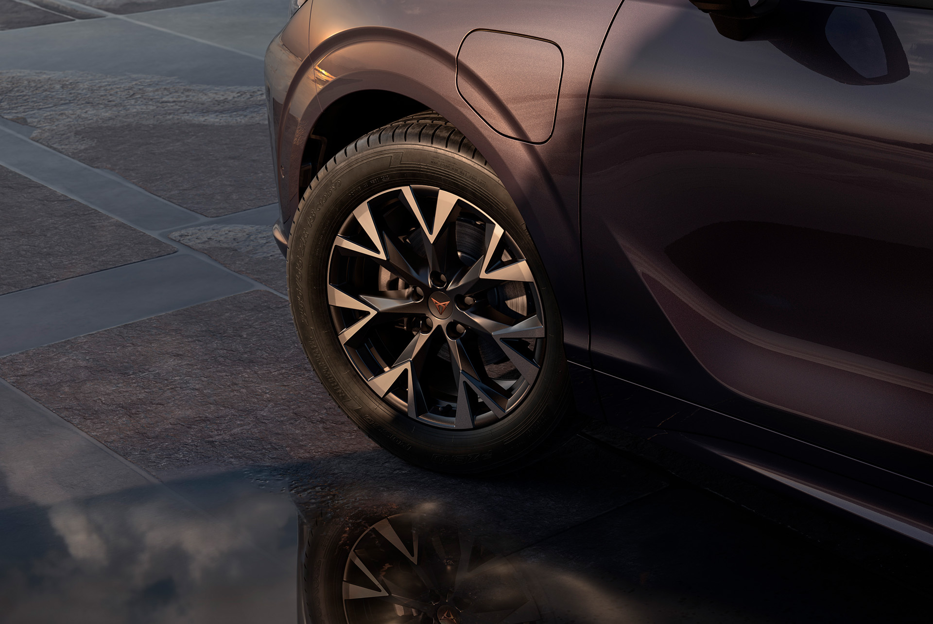 18 inch atomic alloy wheel on the new cupra terramar, in black with copper accents. Background includes a tiled pavement and part of the car's glossy, dark body. 