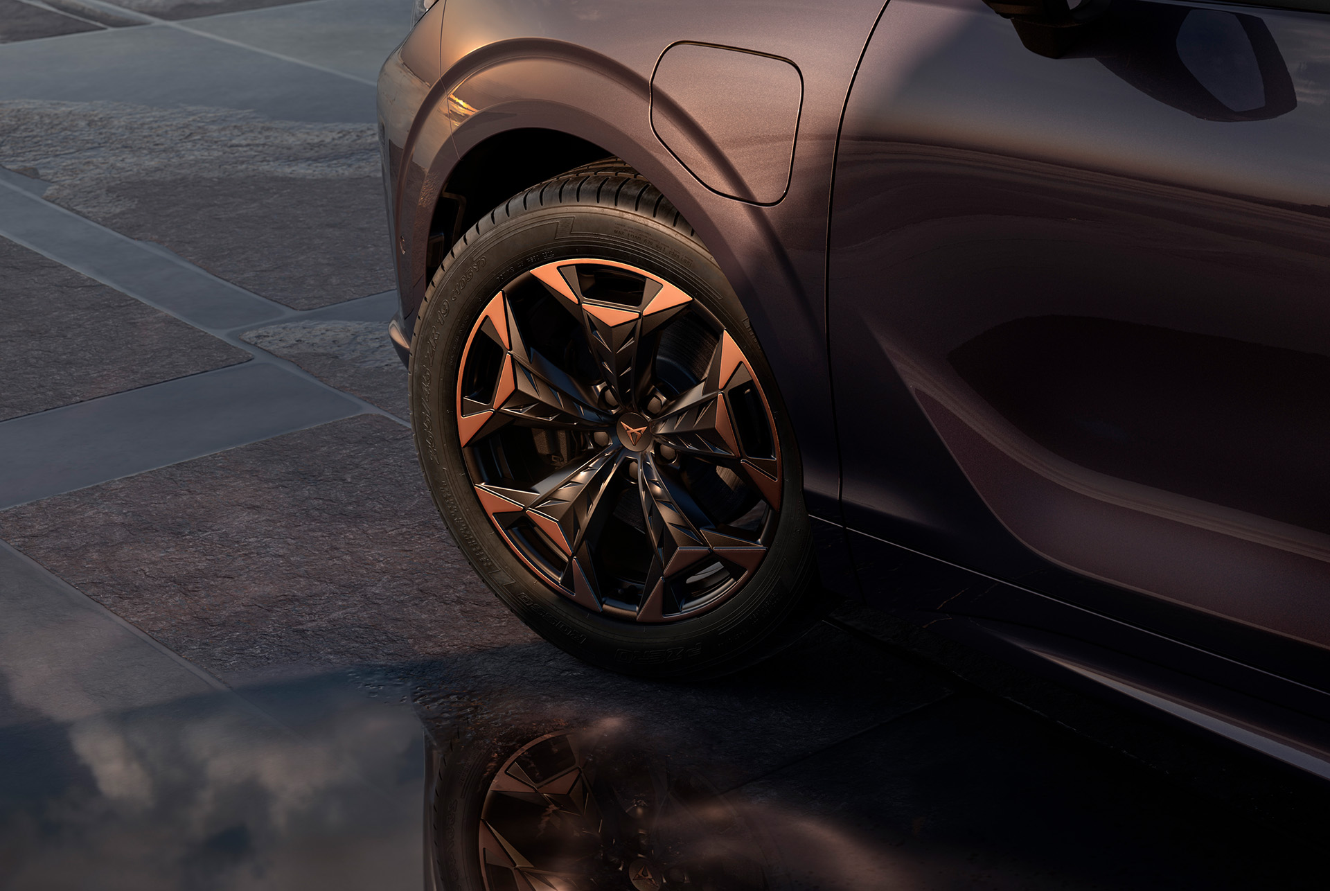 19 inch cosmic copper alloy wheel on the new cupra terramar, in black with copper accents. Background includes a tiled pavement and part of the car's glossy, dark body.